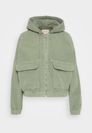 Jachetă din corduroy verde cu glugă, închidere frontală cu fermoar, două buzunare mari în față și elastic la tiv și la manșete pentru o siluetă ajustată.