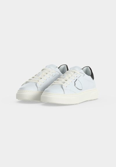 Paire de baskets blanches basses avec semelles épaisses blanches, lacets blancs et accents noirs au talon, placées côte à côte sur un fond uni.