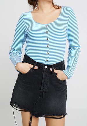Un haut à manches longues, rayé bleu et blanc, avec un col bateau et une fermeture à boutons, associé à une jupe en denim noir avec un ourlet effiloché.