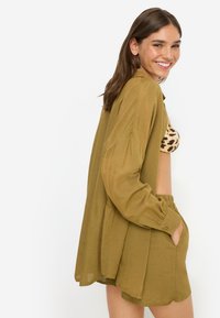 Πουκάμισο από ελαφρύ ύφασμα σε ελιά πράσινο χρώμα με μακριά μανίκια και γιακά, συνδυασμένο με σορτς στο ίδιο χρώμα, με ελαστική μέση και πλαϊνές τσέπες.