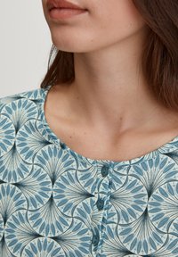 Top a maniche corte, con motivo blu e floral, scollo rotondo e quattro bottoni frontali. Tessuto morbido.