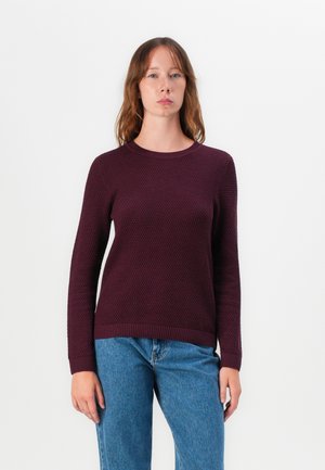 Pull en tricot bordeaux avec un motif texturé, col rond, et bords-côtes aux poignets et à l'ourlet. Associé à un jean bleu clair à jambe droite.