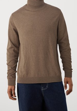 Brauner Rollkragenpullover mit langen Ärmeln, gerippten Bündchen und Saum, aus weichem Material. Getragen über dunkelblauer Jeans.