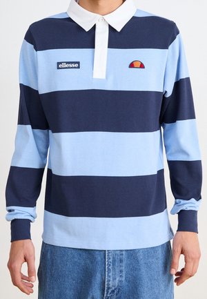 Mann trägt ein langärmeliges Rugbyshirt mit breiten horizontalen Streifen in Marineblau und Hellblau, weißem Kragen und Markenlogos auf der Brust, kombiniert mit blauen Jeans.