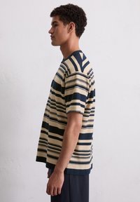 Striped knit t-shirt in beige with navy horizontal stripes, short sleeves, round neckline, slightly loose fit, and side slits at hem.