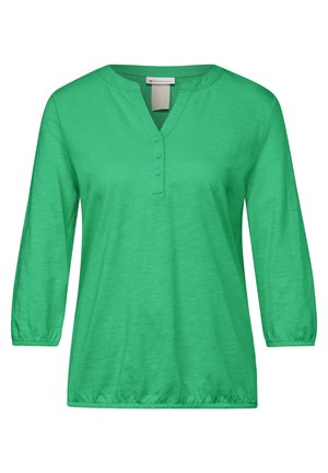 Top verde de manga larga con escote en V y tapeta de botones. Tejido suave y ligero con dobladillo elástico. Diseño sencillo, sin patrones ni acentos.