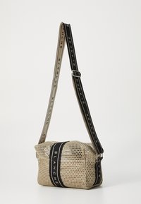 Borsa a rete beige con forma rettangolare morbida. Caratterizzata da manici neri e beige con testo stampato e chiusura a zip.