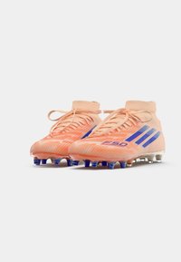 Botas de fútbol naranjas con acentos azules, un upper texturizado y un diseño de tobillo alto. Incluyen cordones y tacos de plástico para tracción.