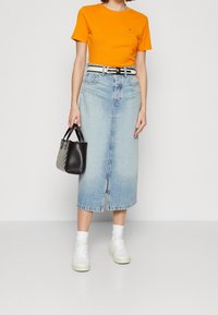 Oranžové tričko s krátkým rukávem v kombinaci se světle modrou džínovou midi sukní, bílými teniskami a černou kabelkou s potiskem.