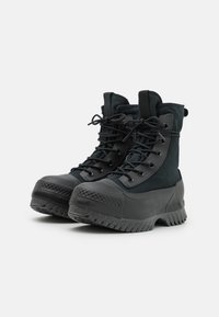 Schwarze wasserdichte Stiefel mit einer strukturierten Gummisohle, Schnürdesign und verstärkter Zehenpartie. Gefertigt aus einer Kombination von Textil- und Gummi-Materialien.