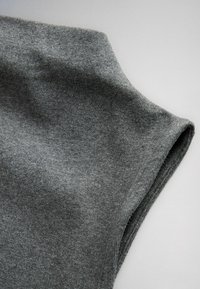 Close-up of gray knitted fabric sleeve with visible texture and fine stitching on a neutral background.