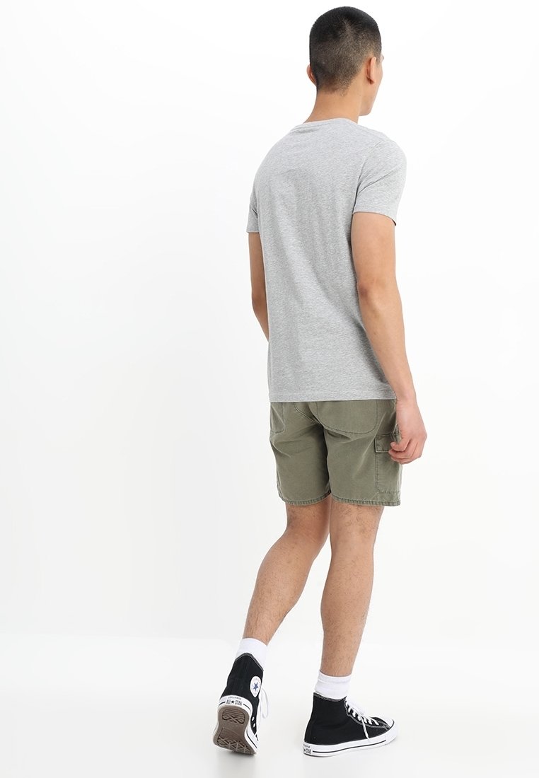 T-shirt gris à manches courtes associée à un short vert olive. La tenue comprend des baskets montantes noires et des chaussettes blanches à la cheville.