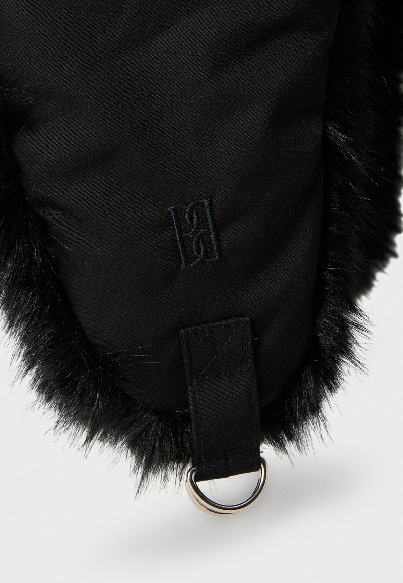 Cappello invernale nero con bordo in pelliccia sintetica, logo ricamato e anello in metallo attaccato a una striscia di tessuto lungo il bordo inferiore.