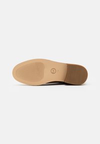 Brown leather shoe sole with a flat design, featuring ridges for grip, a rounded toe, and a subtle logo imprint.