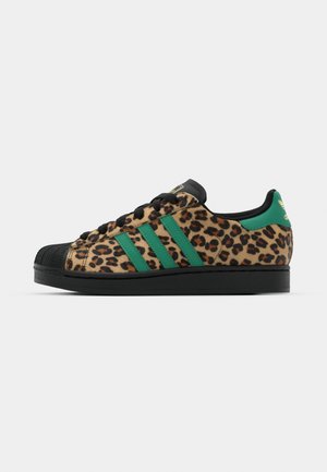Zapatillas de ante con estampado de leopardo, con puntera de goma negra, franjas verdes y suela negra. Cuenta con un diseño de cordones y un cuello acolchado.