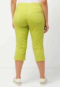 Limoengroene capri-broek met een rekbare tailleband, twee achterzakken en een rafelrand, gecombineerd met witte schoenen.