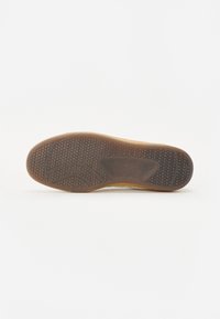 Sko såle med teksturert brun gummi, med et mønstret dekkdesign og en gjennomsiktig side, som forbedrer grep og fleksibilitet.