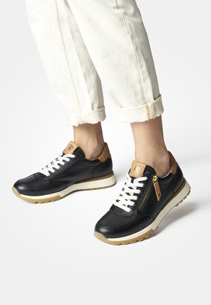 Baskets en cuir noir avec des lacets blancs et une fermeture éclair sur le côté. Présentent un accent beige sur le talon et une semelle texturée beige clair.