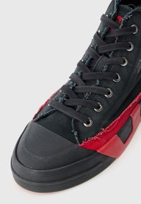 Zwarte canvas sneaker met rode accenten, geg textureerde rubberen zool, metalen oogjes en rafelige randen voor een versleten uitstraling. Vetersluiting.