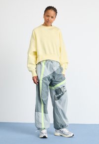 Felpa gialla corta con un piccolo logo, abbinata a pantaloni da jogging grigi con strisce neon e un grande logo sulla gamba.