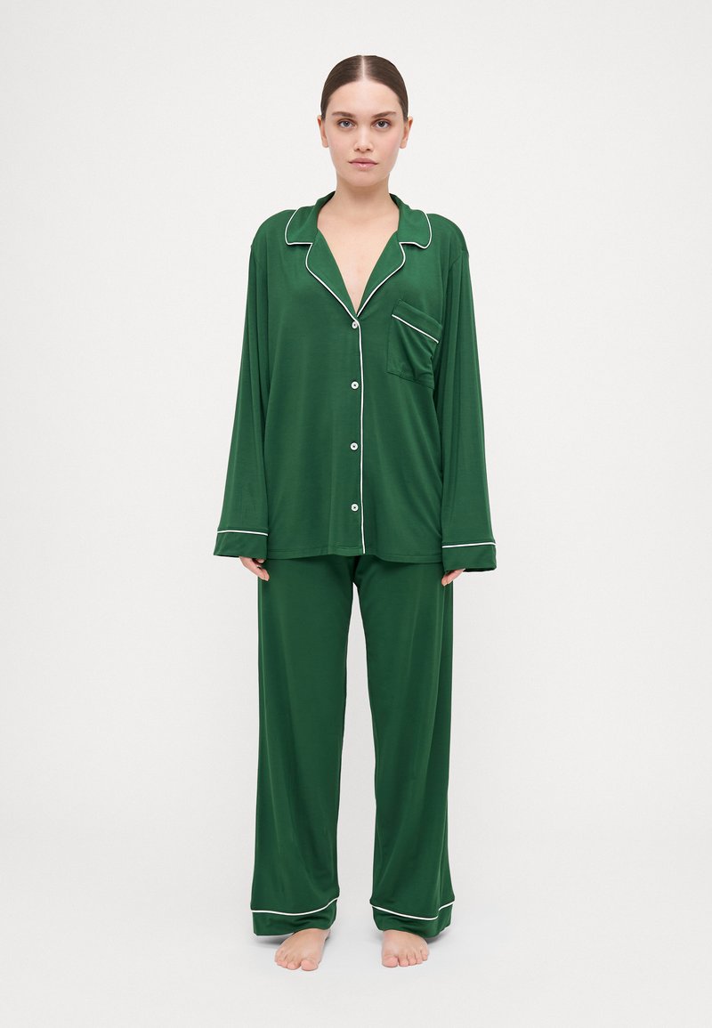 Green pajama set with long sleeves and pants, featuring white piping along the collar, pocket, and cuffs. Soft, smooth fabric.