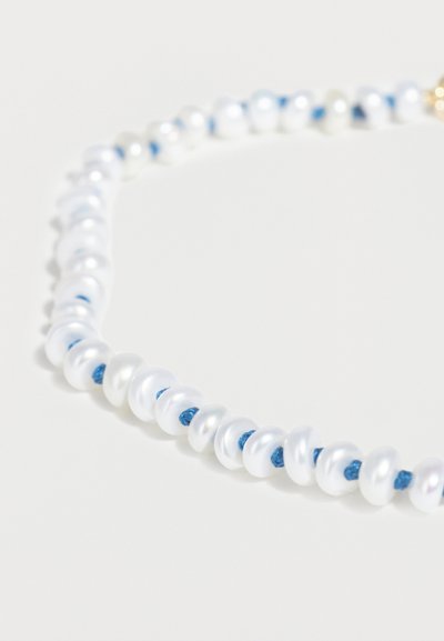 Λευκά ανώμαλα μαργαριτάρια περασμένα σε μπλε κορδόνι, σχηματίζοντας μια κοντινή όψη ενός λεπτού κολιέ σε φωτεινό φόντο.