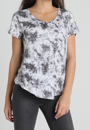 Kvinde iført en sort- og hvid tie-dye t-shirt med korte ærmer og en forlommer, kombineret med mørkegrå jeans.