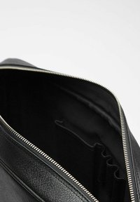 Indvendig af en sort lædertaske med lynlåslukning, der har en glat tekstur og flere rum til organisering.