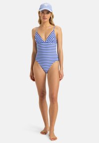 Maillot de bain une pièce rayé en bleu et blanc avec un décolleté en V profond et des bretelles fines. Accompagné d'une casquette bleu clair.