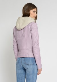 Lilla læderjakke med en beige hættetrøje. Den har en tætsiddende pasform, synlige sømme og metalliske detaljer ved taljen. Bagudsigt.