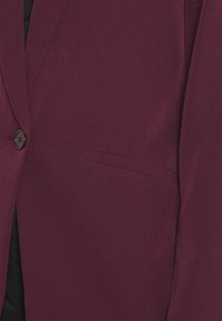 Bordowa marynarka na guziki, z pojedynczą kieszenią na piersi i gładką, teksturowaną tkaniną. Charakteryzuje się eleganckim, dopasowanym krojem.