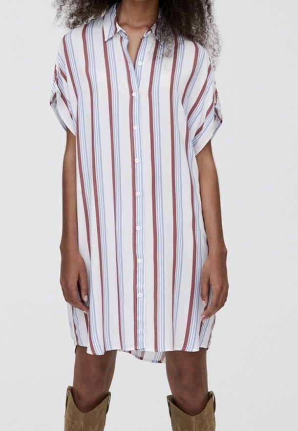 Robe à manches courtes rayée en blanc, avec des rayures verticales rouges et bleues, dotée d'une fermeture à boutons sur le devant et d'une coupe ample, associée à des bottes marron montant jusqu'au genou.