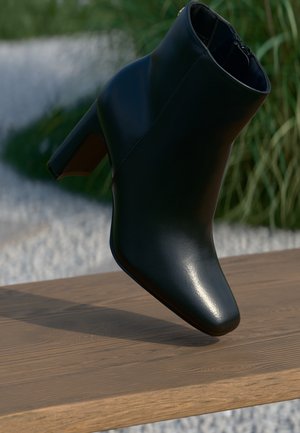 Black leather ankle boot with block heel placed on wooden bench outdoors with grass and white stones in the background.
