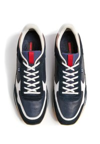 Marineblaue und weiße Sneakers mit Obermaterial aus Mesh und Wildleder, weißen Schnürsenkeln, Gummisohle und einem roten Akzent auf der Zunge.