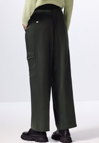 Wijde cargo-broek in donkergroen stof, met een elastische tailleband, zijzakken en een stijlvolle, gladde textuur.