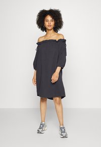 Vestido cinza escuro, com decote off-the-shoulder, gola frisada, mangas três quartos e fendas laterais. Combinado com sapatilhas cinzas.