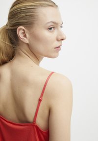 Top rojo sin mangas con tirantes delgados, textura suave y un ajuste relajado. El fondo es blanco liso, lo que enfatiza el color de la prenda.