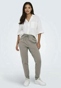 Leichte, kurzärmlige weiße Hemdbluse mit einer Brusttasche, kombiniert mit beigen Sweatpants mit Kordelzug und weißen Turnschuhen.