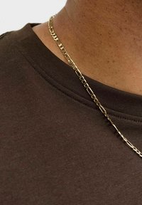 Smeđi pamučni T-shirt s okruglim izrezom, uparen s tankim zlatnim lancem ogrlicom koji sadrži male međusobno povezane segmente.