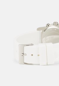 Vit silikonarmband med en silvermetalspänne, med en slät yta och en minimalistisk design. Baksidan visar detaljer om klockhöljet.