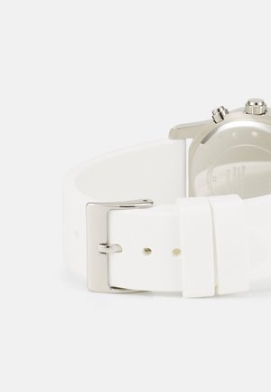 Bracelet en silicone blanc avec une boucle en métal argenté, présentant une texture lisse et un design minimaliste. Le côté arrière montre les détails du boîtier de la montre.