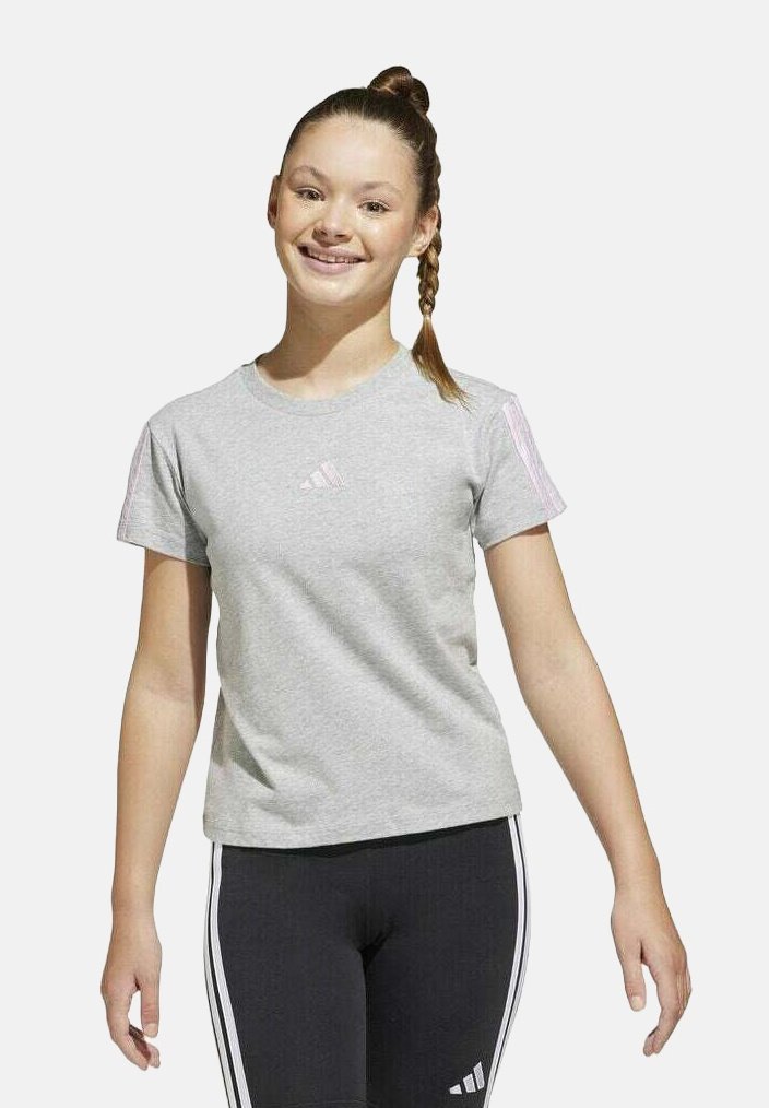 Camiseta gris de manga corta con cuello redondo y logotipo de Adidas en el pecho. Combinada con leggings negros que tienen rayas blancas.