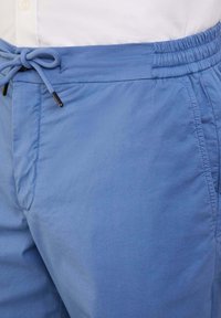 Pantaloni corti azzurri chiari con vita elastica e chiusura con cordoncino, tasche laterali e una texture di tessuto liscia e leggera.