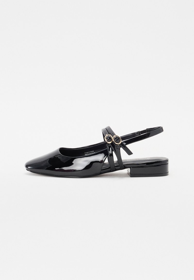 Scarpa slingback in pelle verniciata nera con punta affusolata, tacco basso e due fibbie circolari decorative sulla cinghia regolabile.