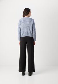 Knit sweater in blue and white marled pattern, relaxed fit, round neck, paired with high-waisted black wide-leg trousers and chunky black shoes.