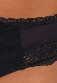 Schwarze Unterwäsche mit einem durchsichtigen Stoffabschnitt und einer Spitzenkante. Verfügt über aufwendige Muster entlang der Kanten und eine glatte Textur.