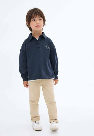 Marineblauer Pullover mit Kragen und drei Knöpfen, kombiniert mit hochgekrempelten beigen Hosen und weißen Sneakers. Baumwollstoff mit weicher Textur.