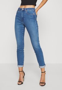 Höga denimjeans i mellanblått, med en kroppsnära design, uppvikta benslut, två framfickor och kopparfärgade detaljer.