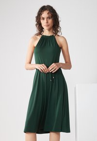 Green dress with a halter neck, gathered neckline, and a drawstring waist. Smooth, lightweight fabric falls to mid-calf length.