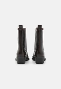 Bottines en cuir marron avec une finition lisse, dotées d'un talon carré et de détails à nervures verticales sur les côtés.